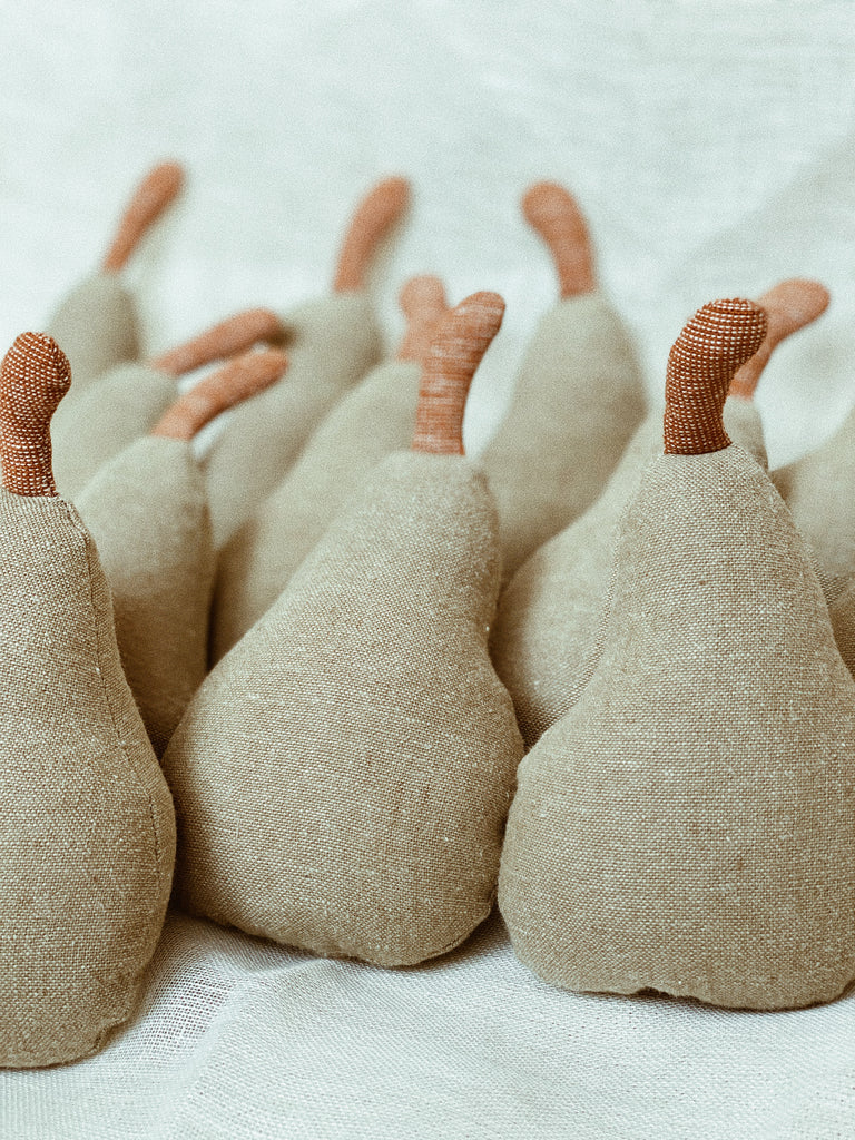 A low-angled, close-up shot of the pear rattles neatly organized in rows. About ten pear rattles are visible in the photo, and on the first three in the front row, the beautiful, slubby texture of the linen fabric is visible.
